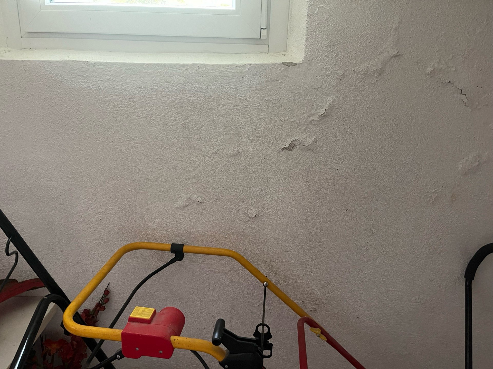 Feuchtigkeitsschäden und Putzablösungen an einer Kellerwand unter einem Kellerfenster