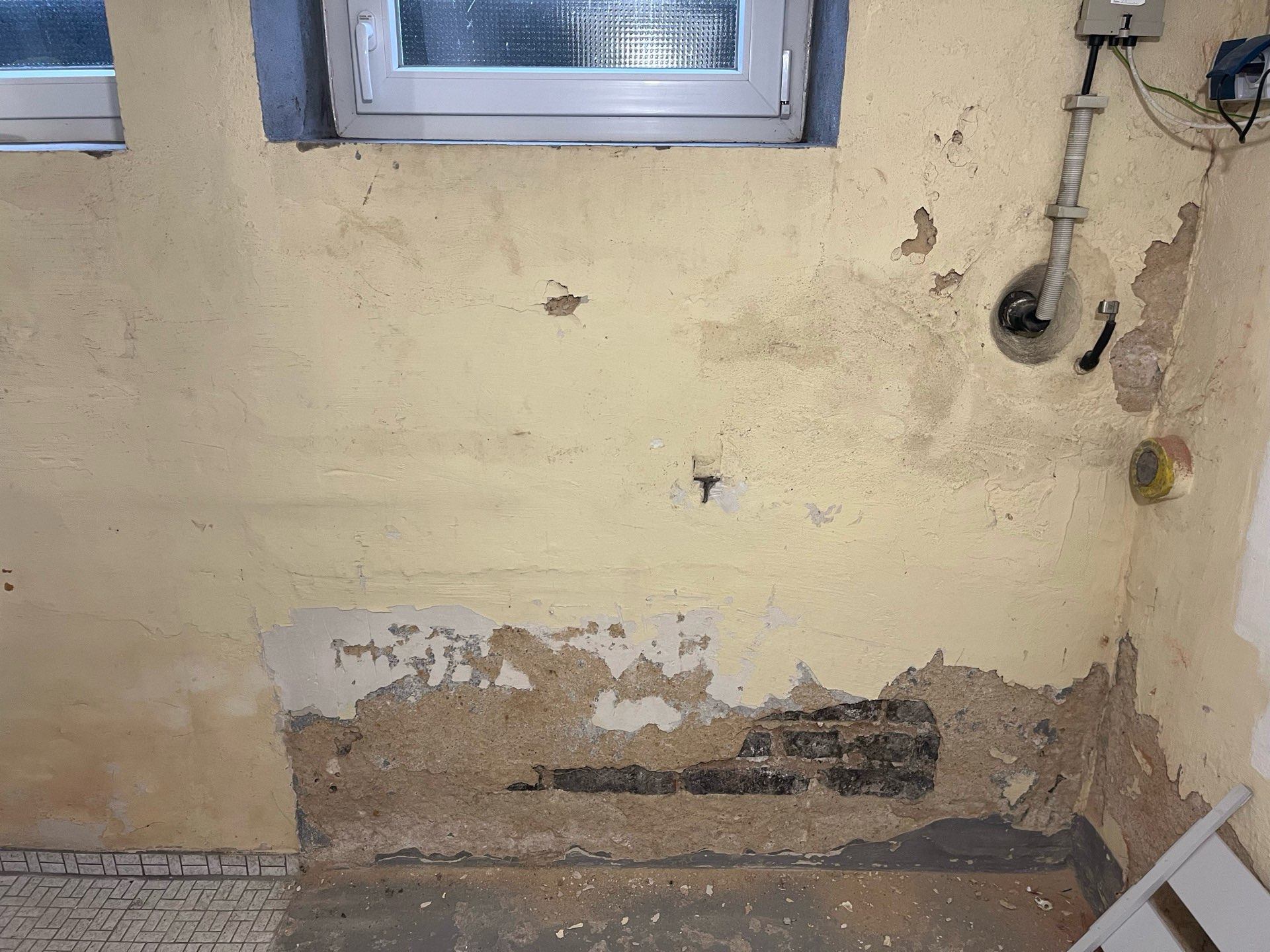 Feuchtigkeitsschäden an einer Kellerwand mit abplatzendem Putz im Sockelbereich